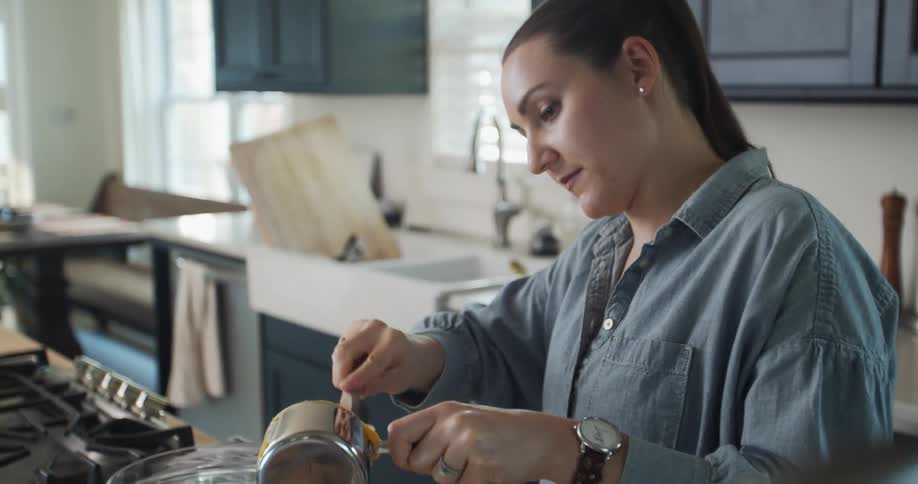 A woman scrapes food out of a measuring cup with a spatula