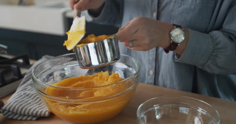 A woman baking at home puts puree in a measuring cup