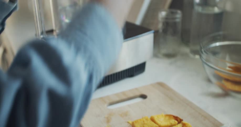 A woman cuts up pieces of pumpkin and adds them to a food processor while cooking at home