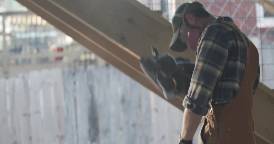 A man in safety glass mask and gloves is turning on a sander to sand wood on a table