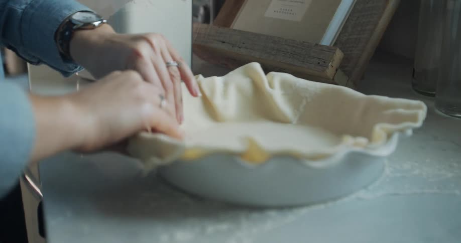 A woman stands at a counter pressing a pie crust in a dish with her hands