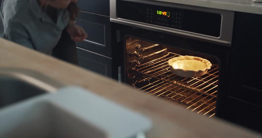 A woman at home puts a pie in the oven and closes the door