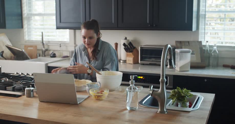 Woman reading a recipe on a laptop at home following the instructions to cook food
