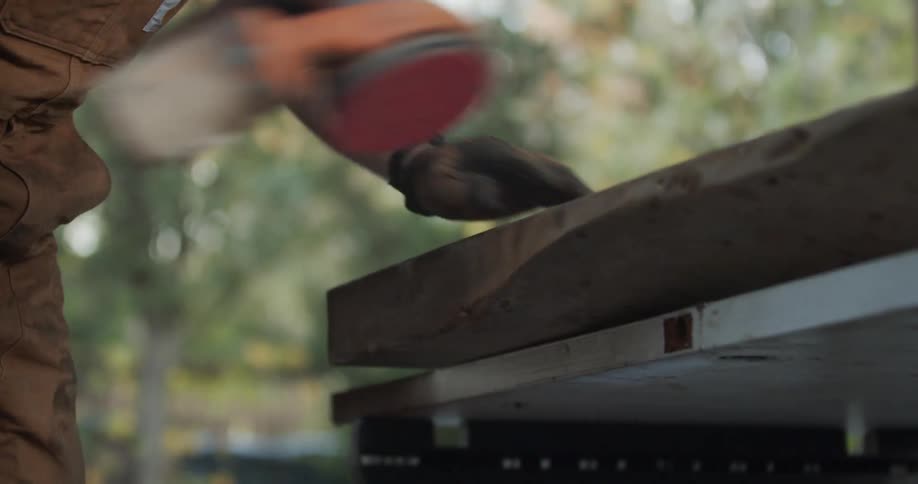 A man is sanding a large piece of wood outside