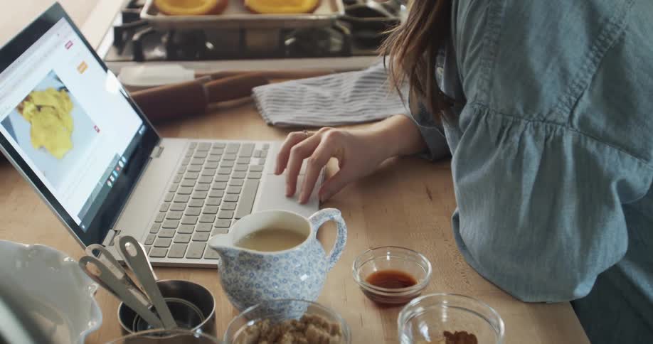 Woman preparing food in the kitchen at home following a recipe on a laptop