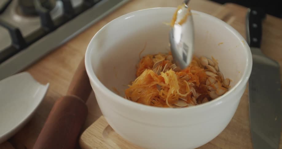 Orange food is spooned into a white bowl sitting on a cutting board next to a knife