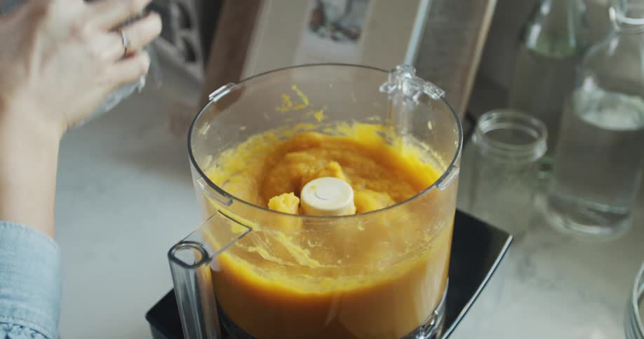 A woman opens a food processor filled with food paste
