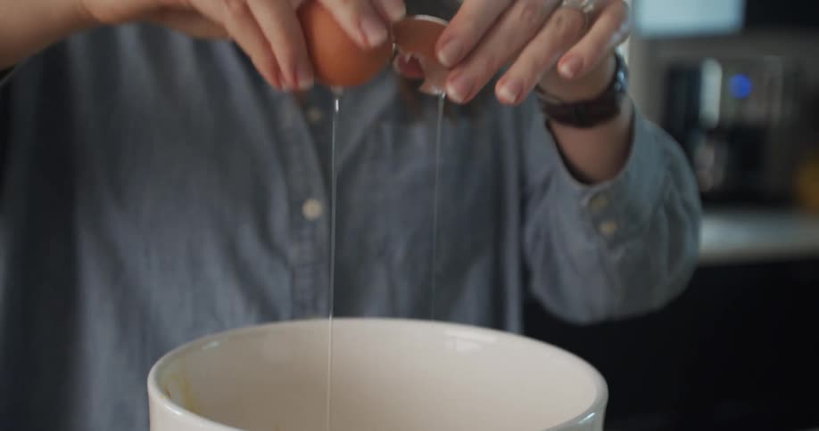 A woman breaks an egg into a white bowl in a kitchen