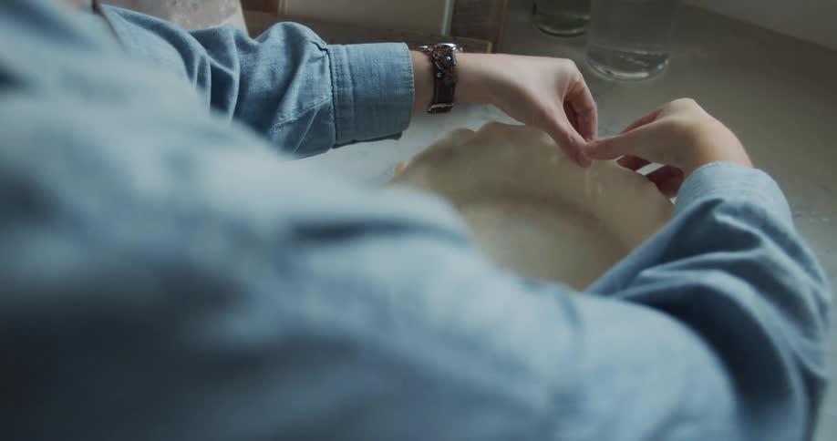 A person places a pie crust on a pan standing at a counter