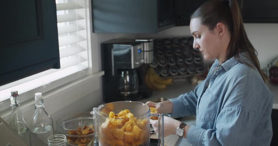 A woman putting food in a food processor