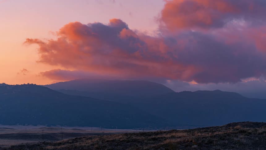 Time lapse of clouds rolling over the mountains in the plains at sunset
