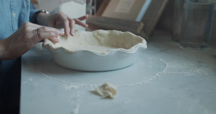 Hands preparing a pie crust in a white pie pan indoors at a kitchen counter top at daytime