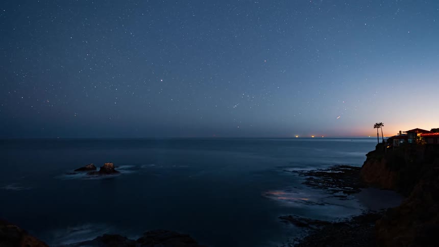 A star filled sky over the ocean as shooting stars move across the sky at dusk