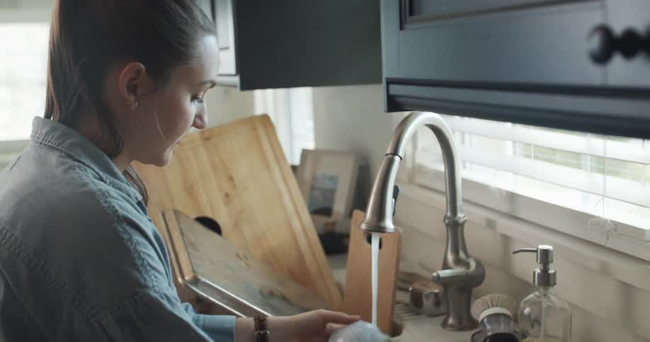 A woman washing dirty dishes in a kitchen sink at home