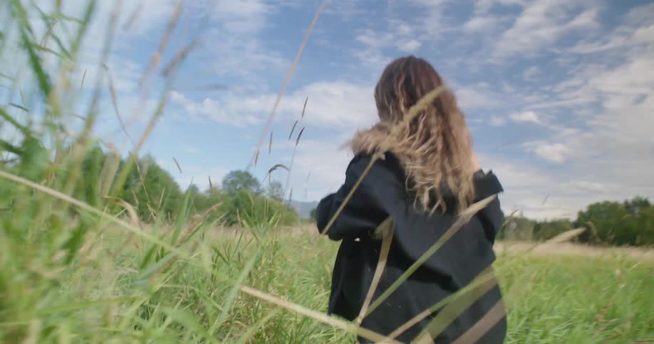A woman running in a grassy field with the sky and clouds in the background