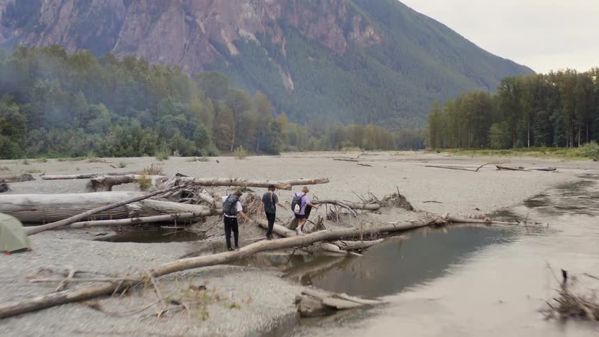 Three teenager walks across a tree trunk over a stream as they hike towards a forest