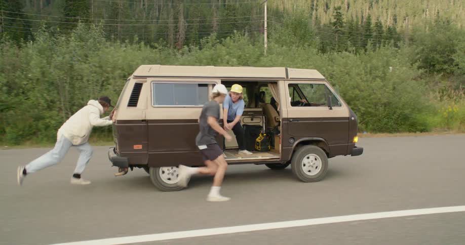 Friends pushing a van on a mountain road run to get inside after it starts