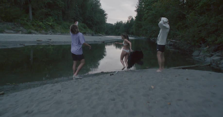 Three young friends running towards a river while undressing at sunset