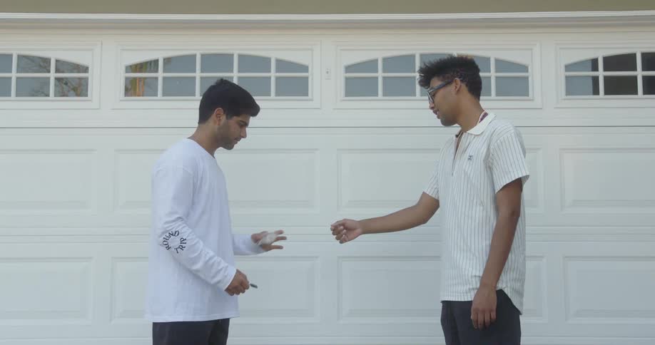 A young man pays another young man for a key before laughing happily