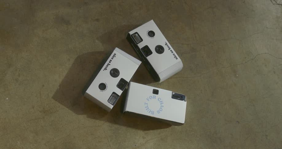 Three white disposable camera get tossed together on a concrete floor