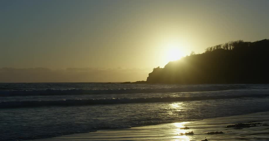 Sun setting as waves roll in over beach with mountains on the horizon