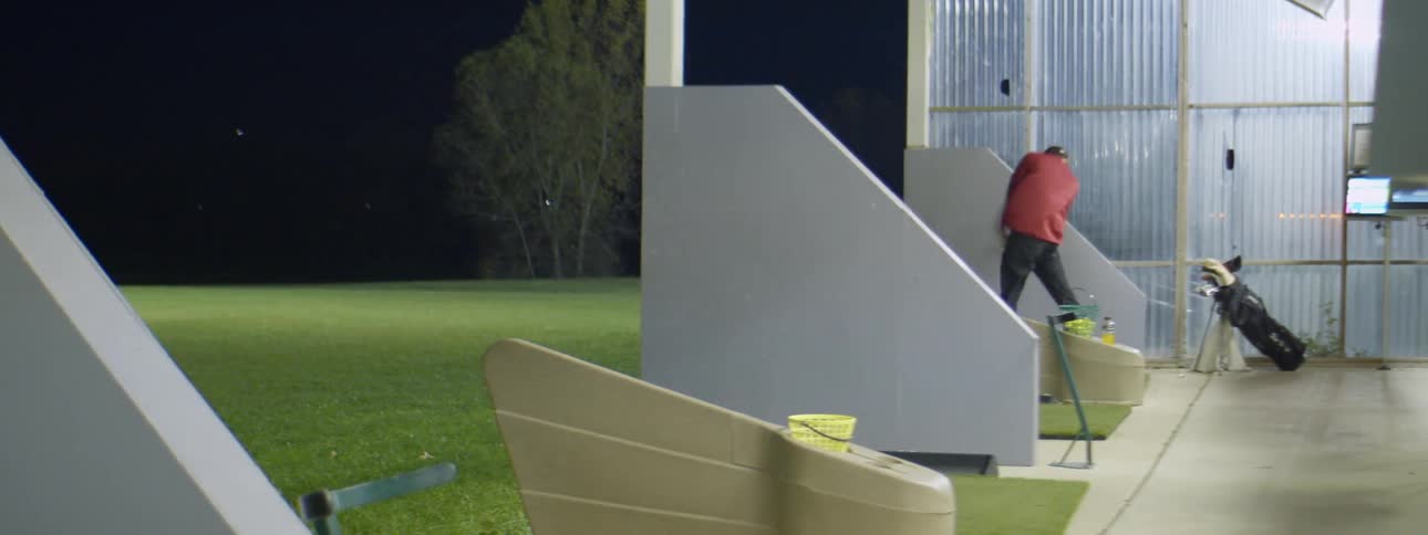 A man hits golf balls at a driving range