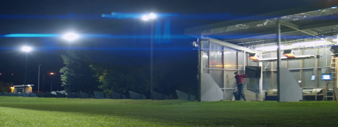 Man practicing golf swings on a golf driving range at night