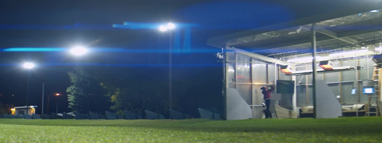 Man practicing golf swing on a golf driving range at night