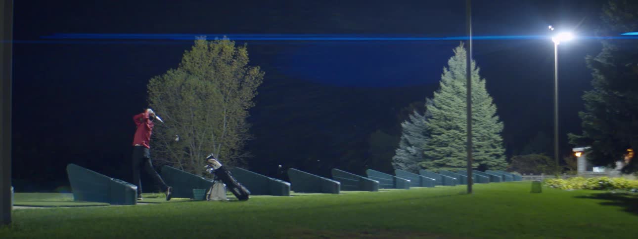 A man hits golf balls outdoors at night