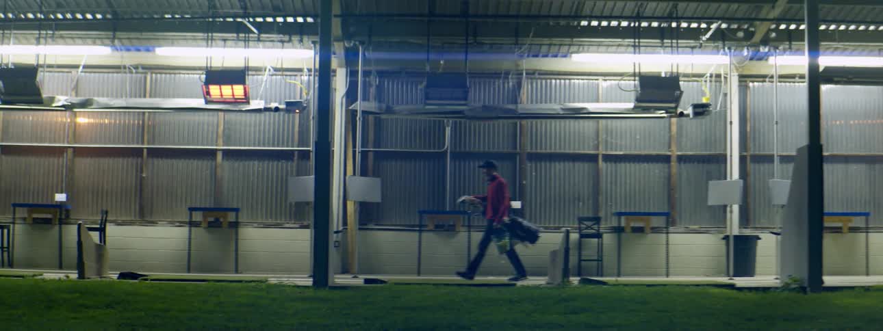 Man carrying golf equipment through a golf driving range at night