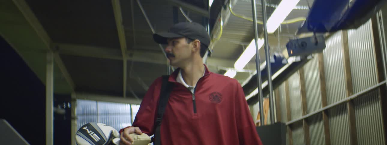 A male golfer carrying a bag with golf clubs walks through a warehouse