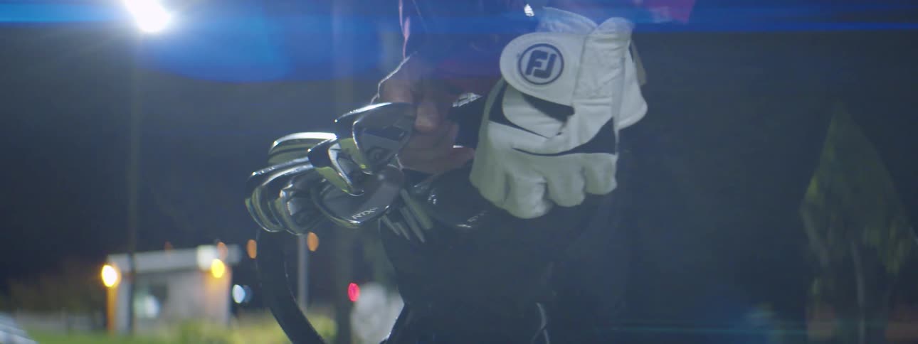 Gloved hand picking out clubs from golf bag at night