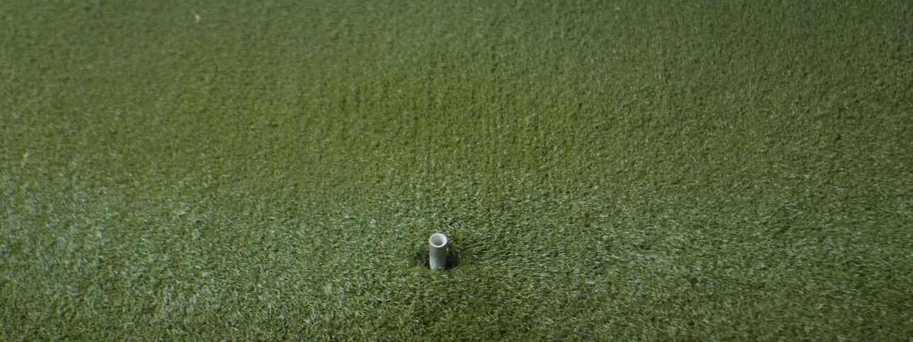 A golfball placed on a tee over artificial grass being hit by a golf iron