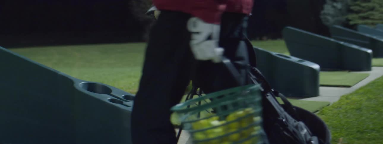 Man carrying golf equipment on a golf driving range at night