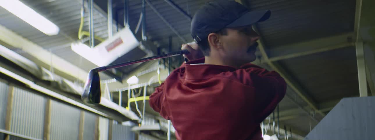 A man is hitting golf balls at the driving range