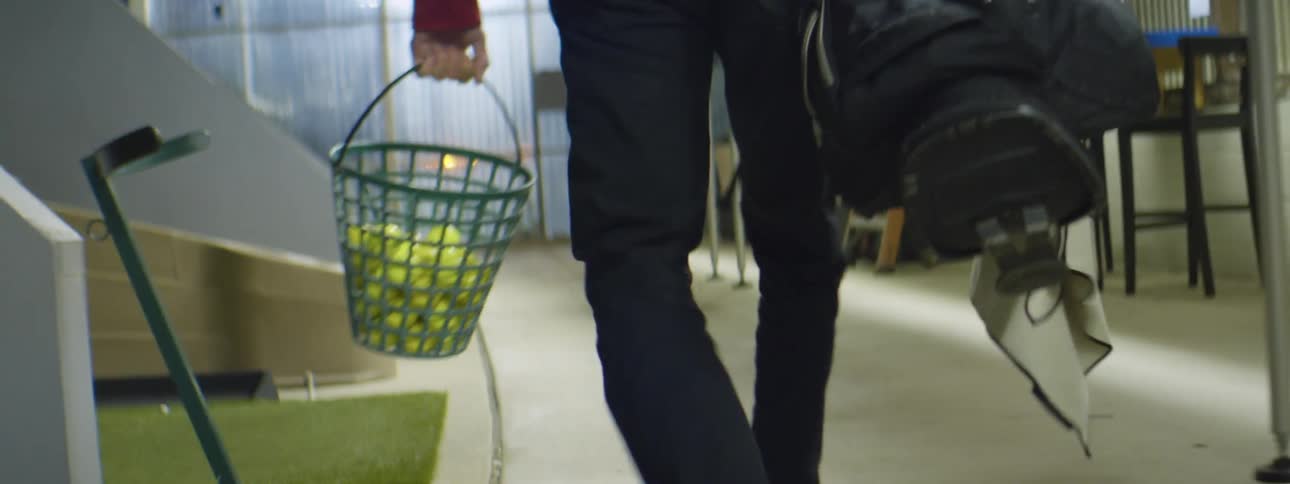 A young man carrying a bucket of golf balls at a driving range