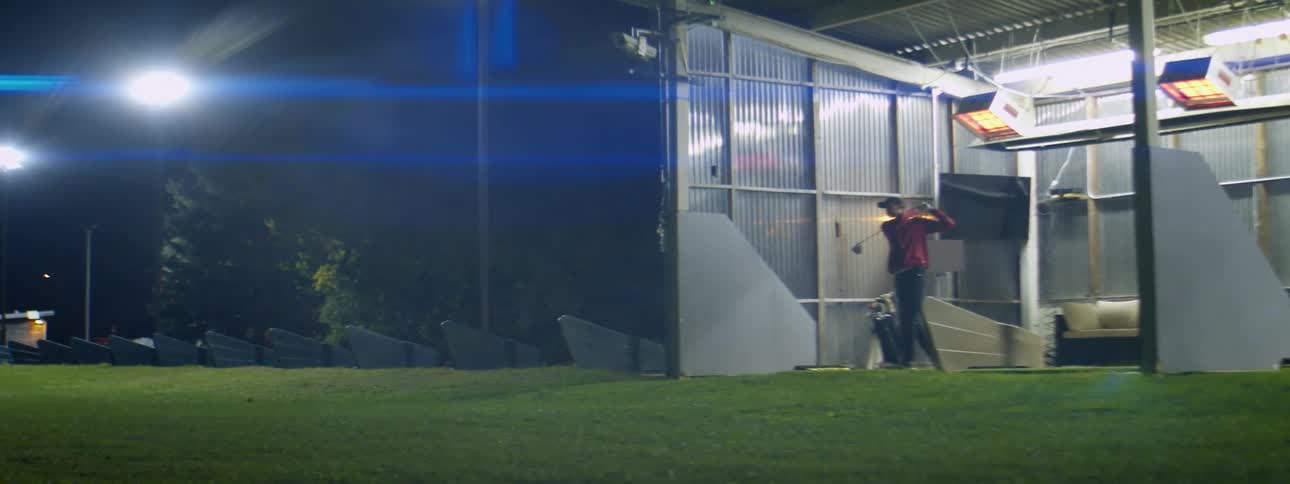 Man practicing golf swings in a golf driving range at night