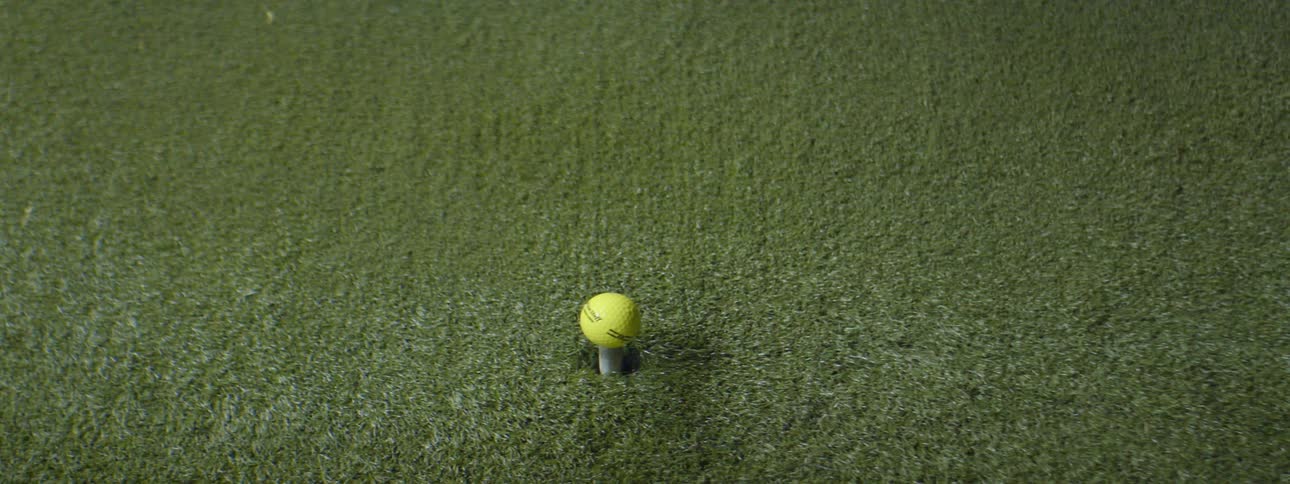 A yellow golf ball sitting on a rubber gold tee is hit with a golf club
