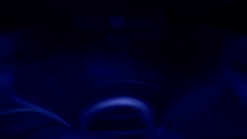 A close up of water draining in a sink to the drain with a blue light