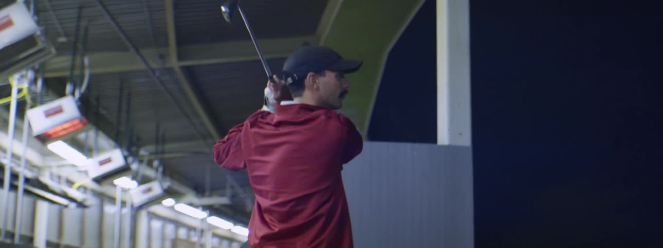 A man plays golf alone at a driving range at night