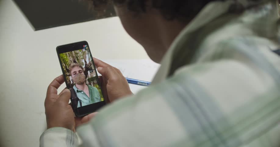 Person with plaid shirt makes video call on smartphone with man wearing shirt and mask