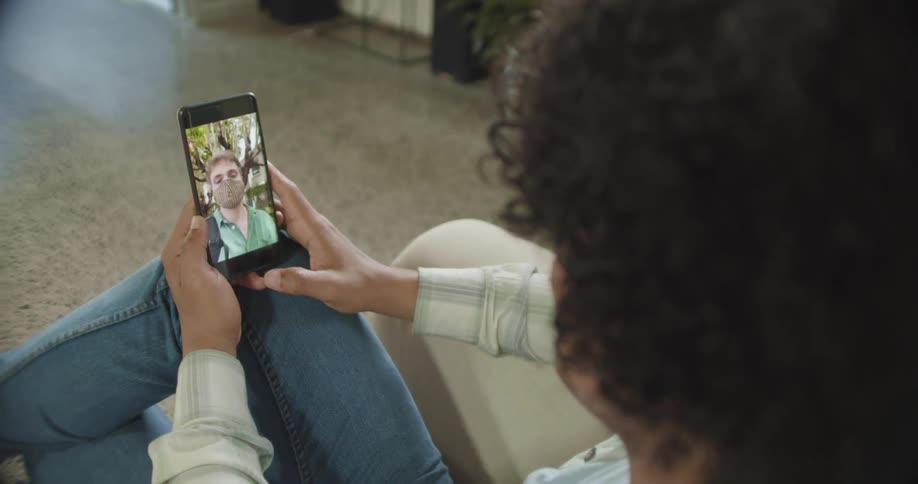 Woman sitting on a chair indoors talking to a man on a smart phone in a video call at daytime