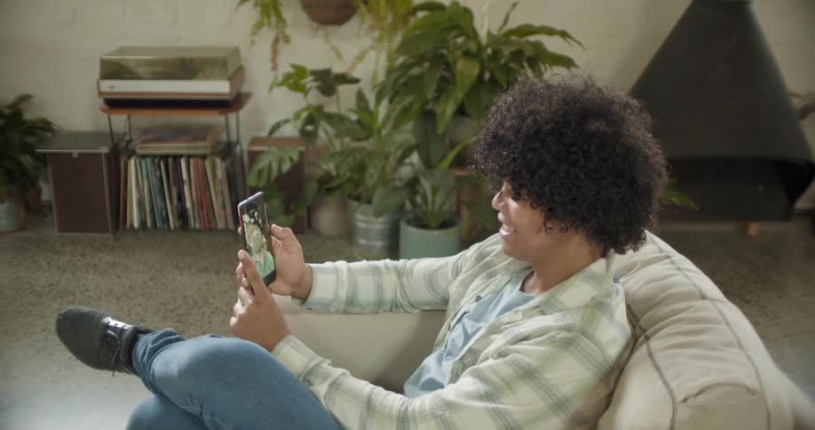 Man sitting in a couch at home smiles while talking on a video call on the smartphone