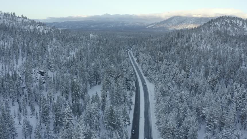 Traffic on forest road on a snowy winter day with snow covered trees and mountains on the horizon