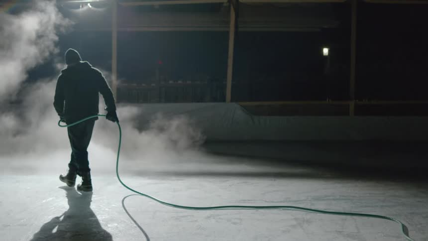 A man with a hat and a hoodie spraying a hose