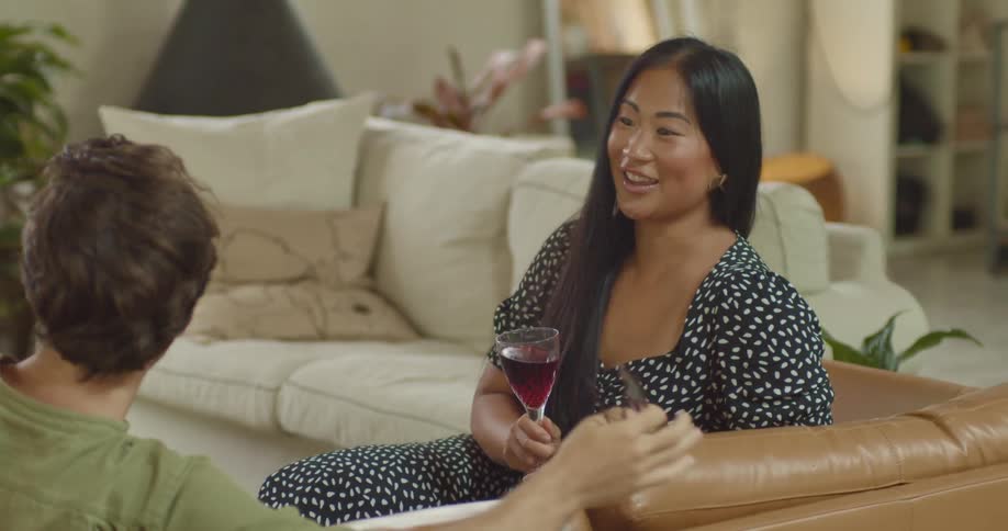 A man and woman sit on a couch and talk and laugh as they have a drink together