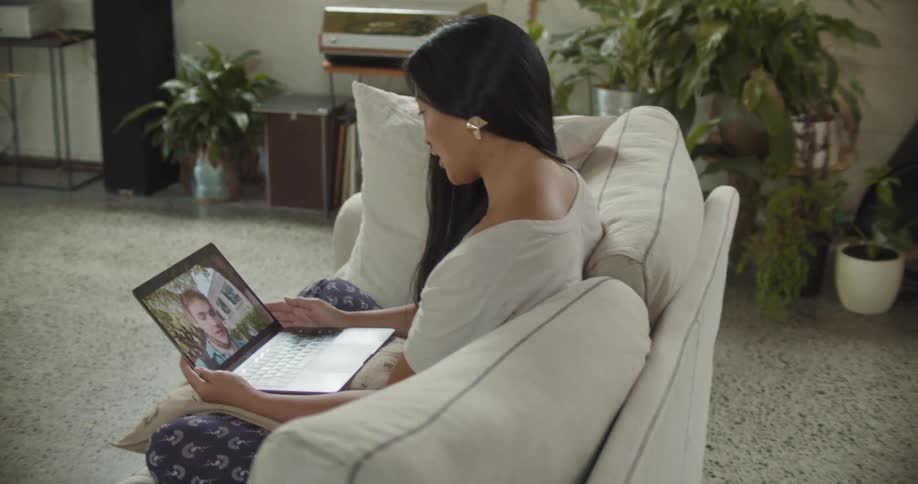 An asian woman sitting on a couch in her living room video calling a caucasian man