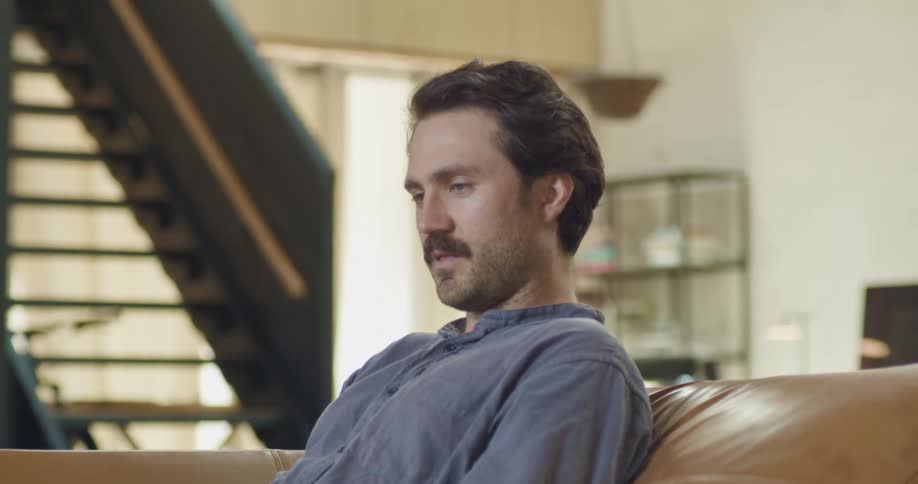 Man sitting in a couch in the living room at home finish a call on a smartphone