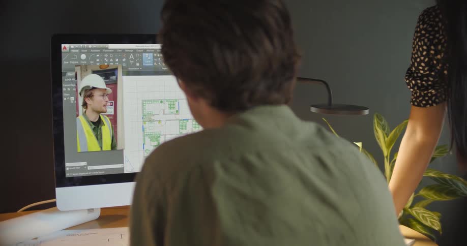 Man and a woman video chatting with a construction worker on a desktop computer at a desk at daytime