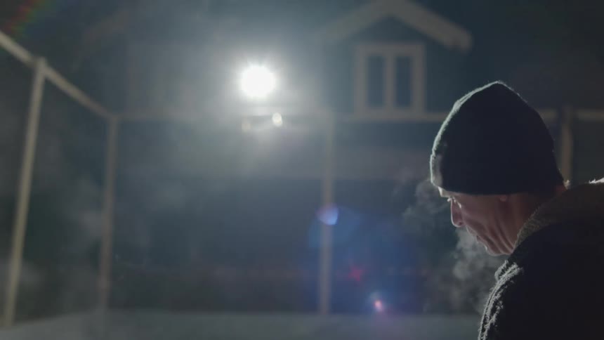 A man is standing in his driveway in front of his house on a cold night